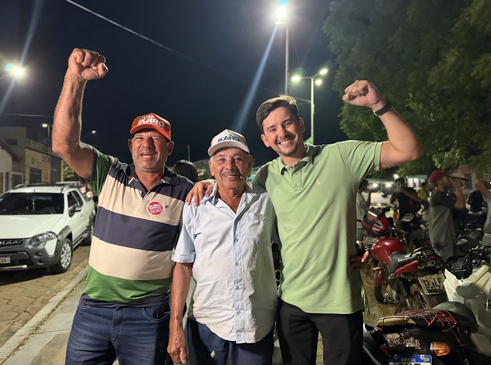 Ikaro Barbosa de punho erguido ao lado de dois apoiadores com bonés da campanha